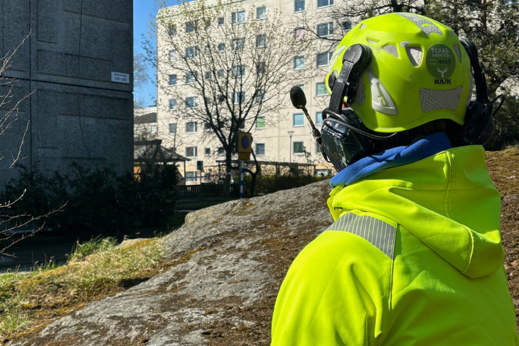 Drönarpilot som tittar upp mot en drönare som rengör fasad utanför bild.